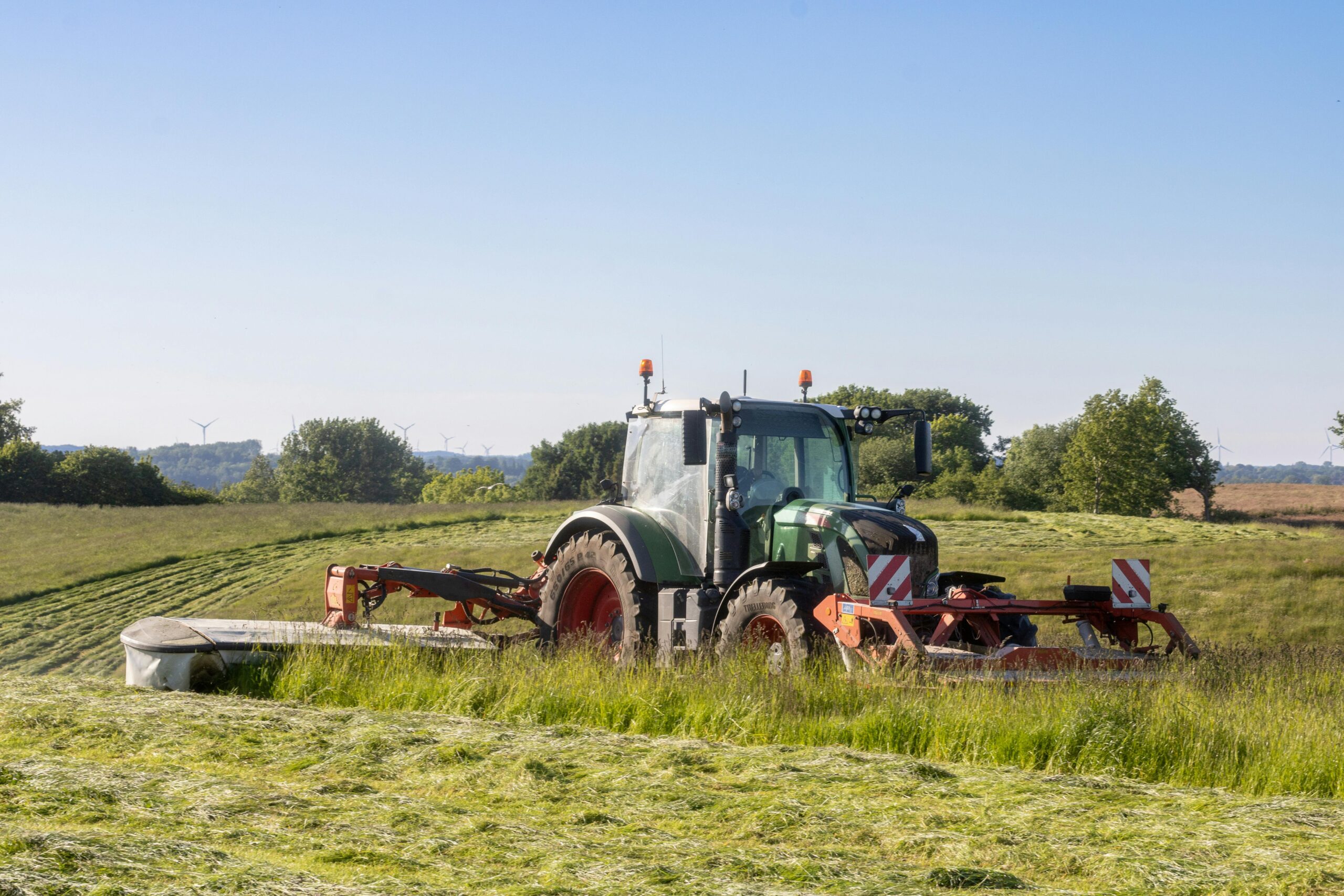 A tractor mowing a lush green field on a sunny day in the countryside.