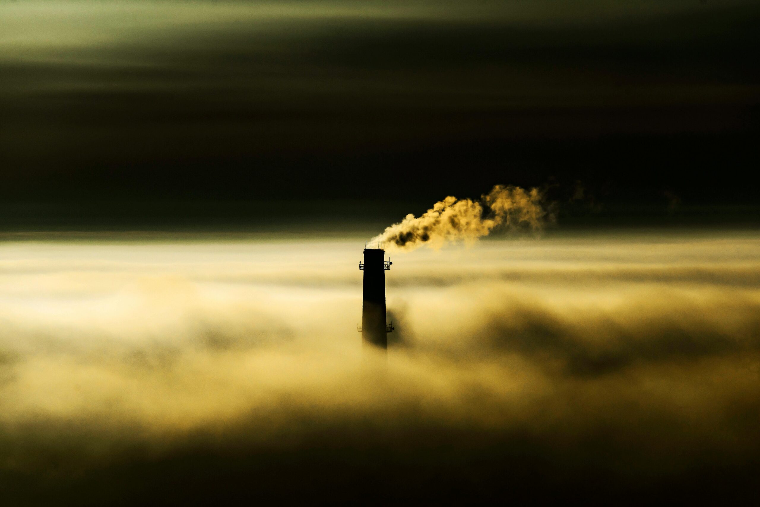 Chimney emitting smoke through dense fog, highlighting air pollution concerns.